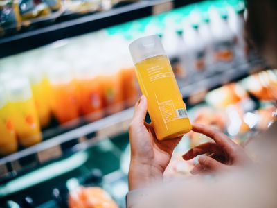 Over the shoulder view of young Asian woman grocery shopping in supermarket. She is reading the nutrition label on the bottle of fresh orange juice