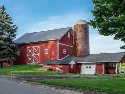 classic red barn with grain silo with large trees and blue sky 