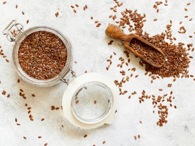 Jar and spoon of raw flaxseeds on textured white background