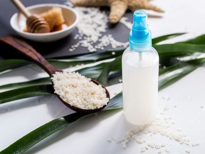 Spray bottle of rice water surrounded by rice and honey