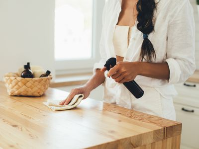 Person cleaning a wooden countertop with spray bottle and cloth