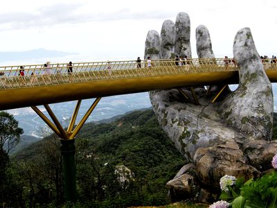 The golden Cau Vang bridge appears to be held by a large stone hand near Danang, Vietnam