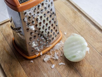 box grater and half an onion on a wood cutting board