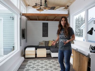 Ana White standing in her tiny home living space with the elevator bed at full height in the background