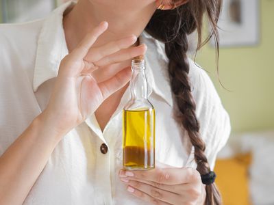 woman holds almond oil bottle with long brown braided hair