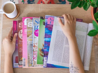 overhead view of hand on multiple magazines spread on a table with coffee cup