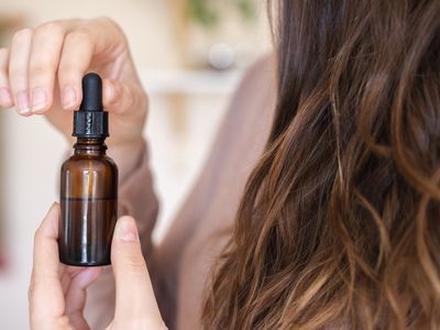 woman with long brown hair removes cap from argan oil in glass bottle