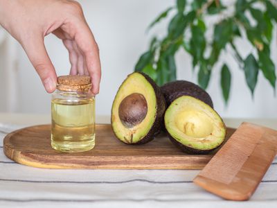 hand touches avocado oil with fresh cut avocados on cutting board