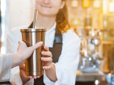 barista hands over coffee in reusable stainless mug