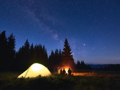 campers under a starry night sky with illuminated tent behind them