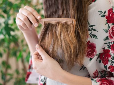 woman in floral robe runs bamboo comb through tangled hair