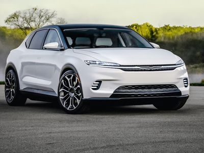 A white Chrysler on a paved road with trees in the backdrop.