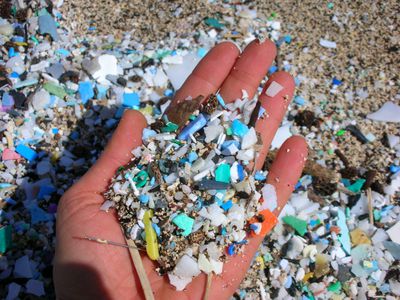 A hand holding a pile of plastic peices and sand