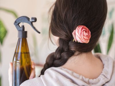 woman's back showing long braided hair with pink rose and DIY hairspray in brown bottle