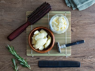 flat lay of raw shea butter in bowls with grooming and hair tools on laminate wood table