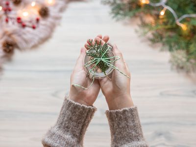 hands hold out glass jar wrapped with twine and fir branch for eco christmas wrapping gift