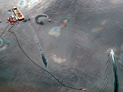 Aerial view of oil-covered water being skimmed by small boat following Exxon Valdez oil spill