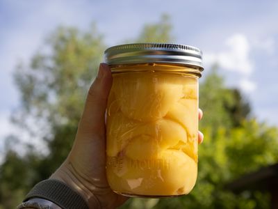 hand holds up large Mason jar of preserved fruits to the sky