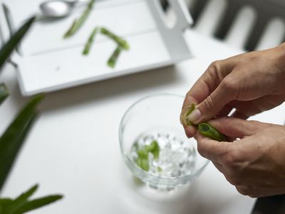 hands squeeze aloe vera gel from plant into glass with ice for eye care