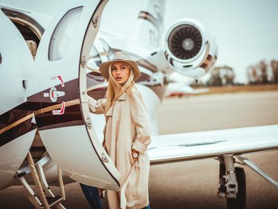 Young rich blonde female entering a private airplane parked on an airport tarmac. 