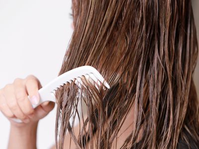 A woman combing her wet hair out with a wide tooth comb.