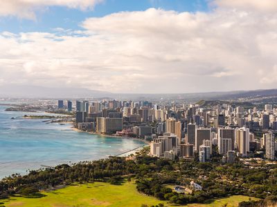 High angle view of skyscrapers in Honolulu along Mamala Bay with lush green trees in the foreground and blue sky with white clouds above on a sunny day 