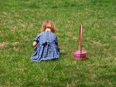 little girl bends over in grass to pick up easter eggs with pink basket