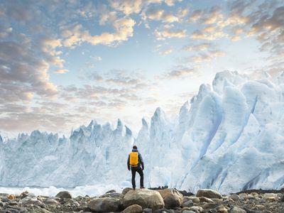 A glacier towers above a hiker at sunset.