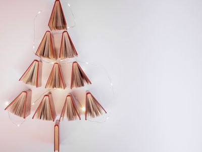 open books are hung on white wall with lights to create Christmas tree