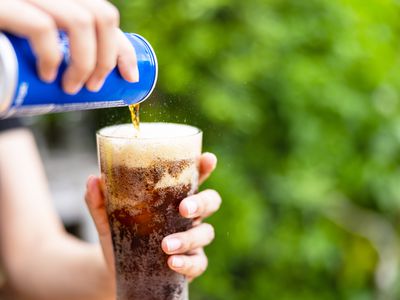 Female hand pouring cola drink from tin to glass