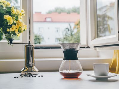 Glass coffee maker with reusable coffee filter on a kitchen table in front of an open window