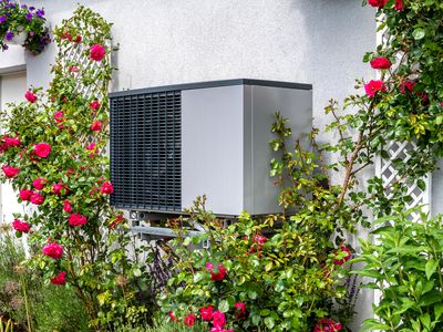 Outdoor unit of a heat pump heating on a house framed by roses