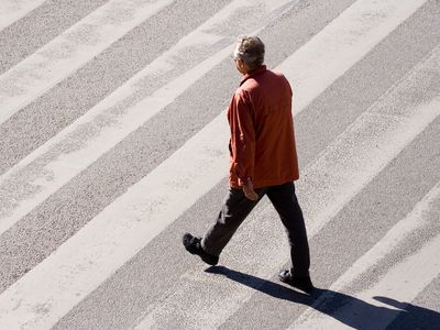 older man goes for walk in empty street using crosswalk with high shadow