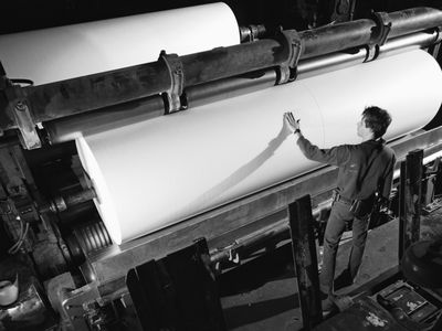 Man inspecting roll of paper in mill,