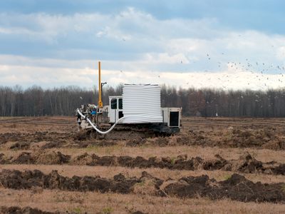 Machinery used to install plastic drainage tile at work in a fallow farm field.