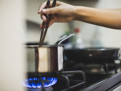 Young woman stirring pan on cooker top with chopsticks