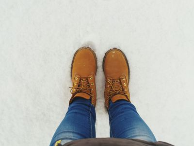 woman stands in powdery snow looking down at brown winter boots