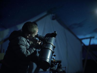 Boy looking through telescope at night