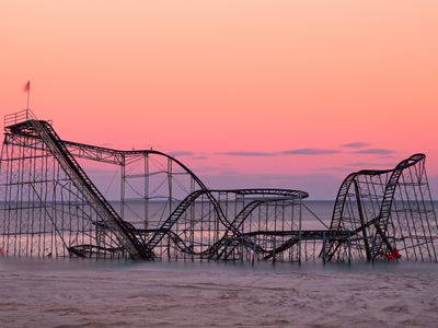 A hurricane-damaged roller coaster sits in the ocean at sunset.