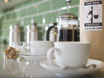 A bag of coffee with a fair trade label on a counter with coffee cups