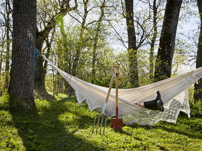 An obscured person in garden boots rests in a hammock with gardening tools resting on the edge