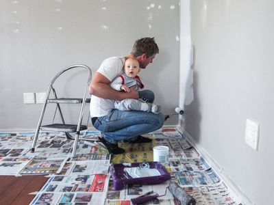 Person holding a baby while painting a wall