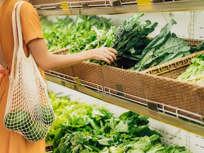 Girl is holding mesh shopping bag with vegetables without plastic bags at grocery shop.