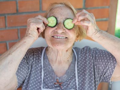 older grandma holds up cucumber slices in front of her eyes