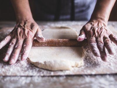 Hands baking dough with rolling pin on wooden table