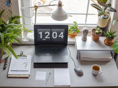 overhead shot of work desk with laptop surrounded by green houseplants near window