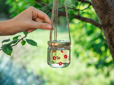 hand touches hanging twine attached to glass jar filled with diy hummingbird nectar