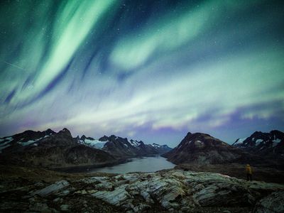 Green and purple northern lights over Greenland fjord