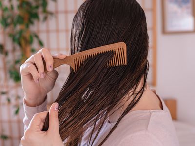 side profile shot of woman combing wet brown hair with brown comb