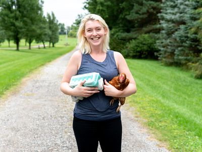 woman smiles while holding egg carton and chicken